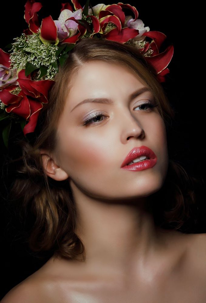 Modèle avec une couronne de fleurs rouges et un jolie maquillage naturel.